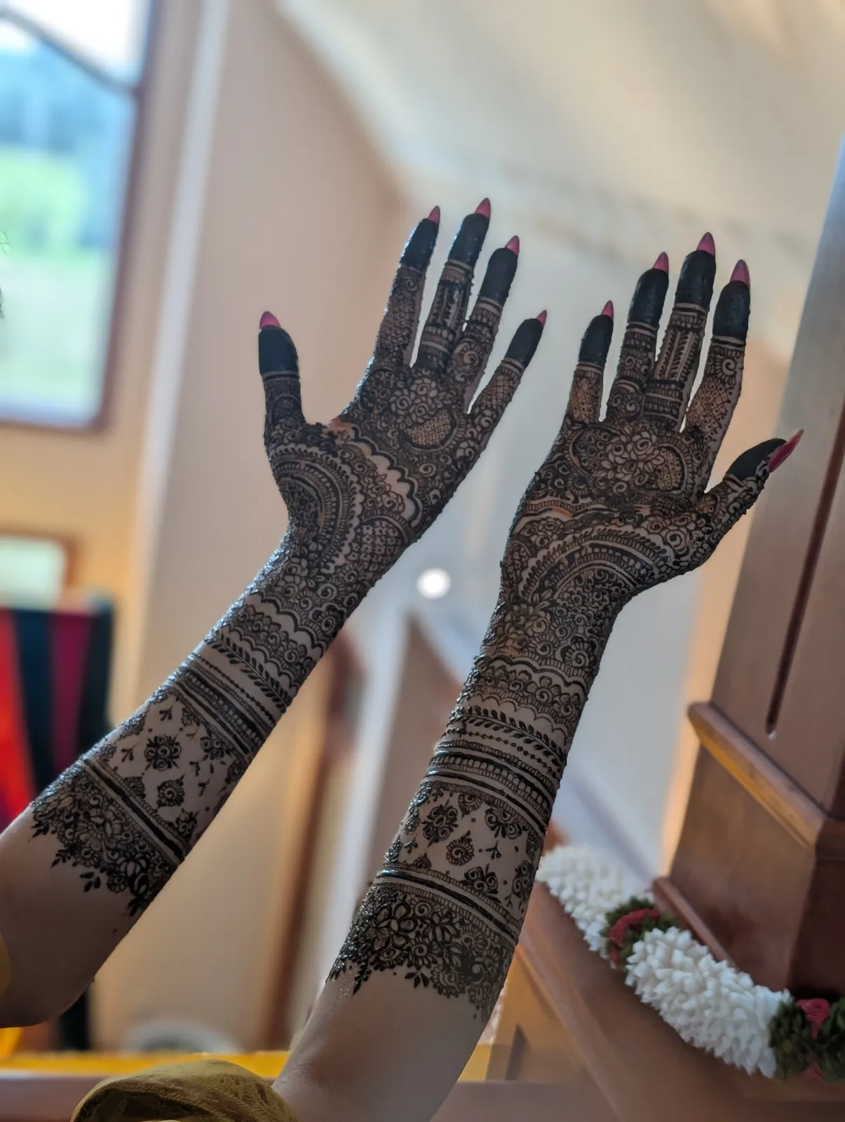 Both arms of finished bridal mehndi held up in soft indoor light