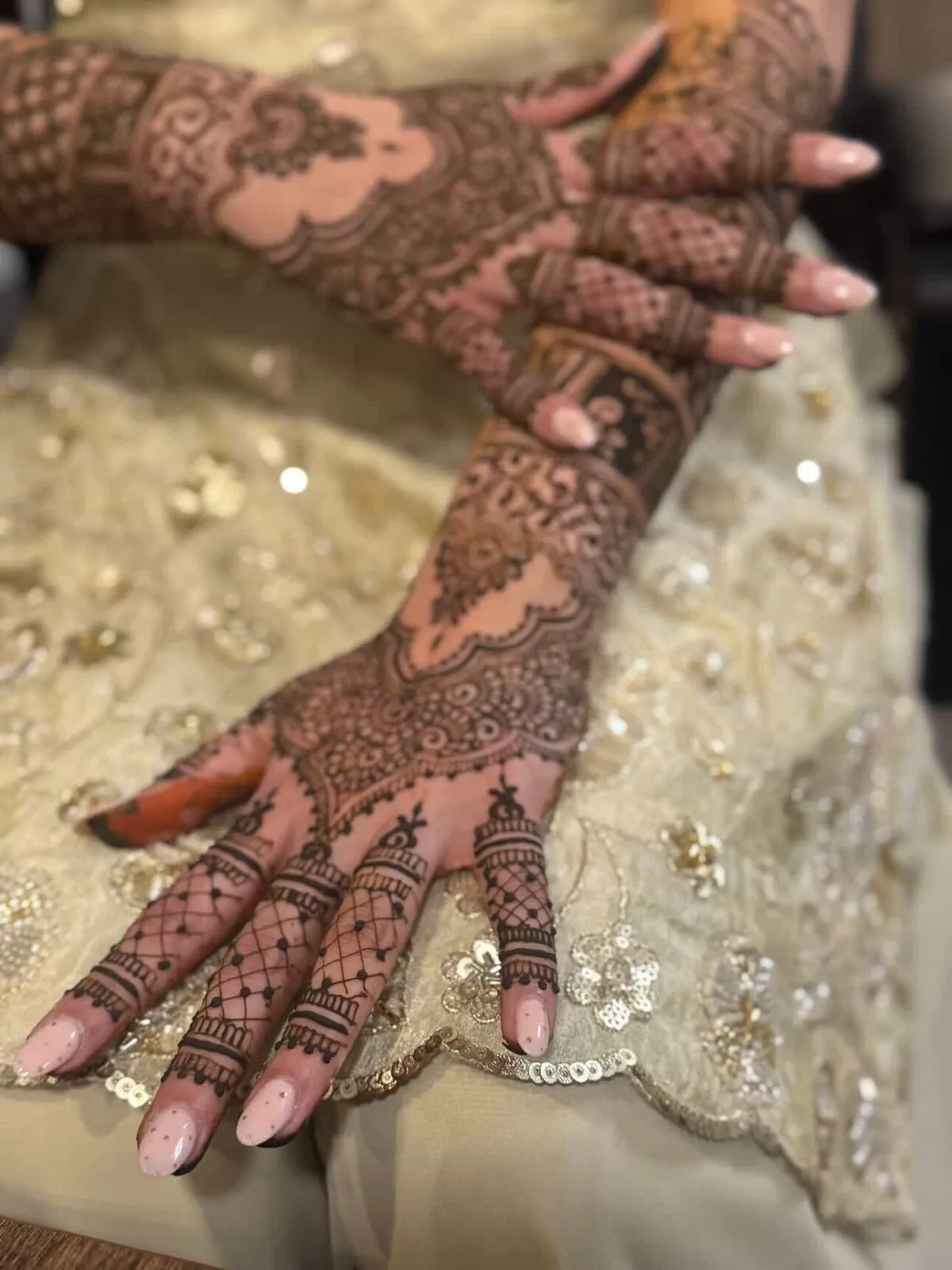 Dense bridal mehndi across the hand and forearm against a cream beaded outfit