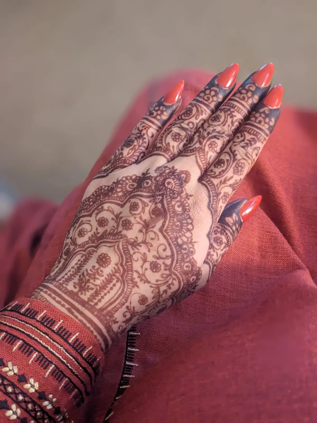 Dense paisley mehndi on the backs of both hands against a red festive outfit