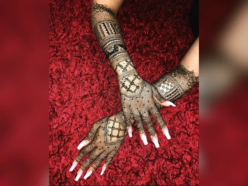 Bride seated in red bridal wear with intricate henna on her hands during application