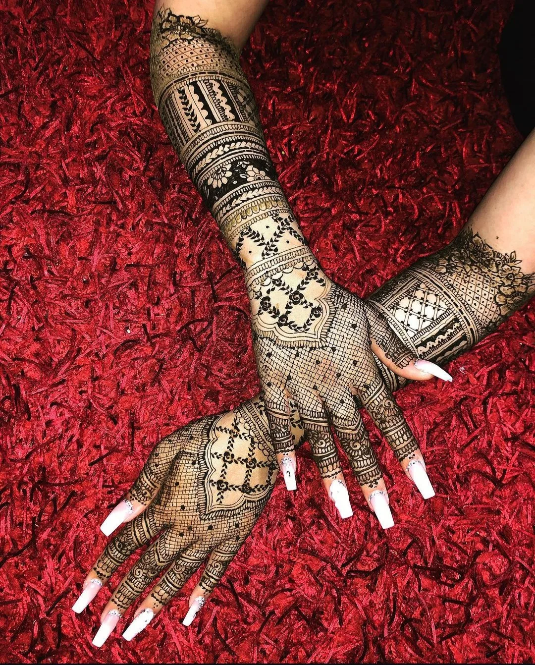 Bride seated in red bridal wear with intricate henna on her hands during application