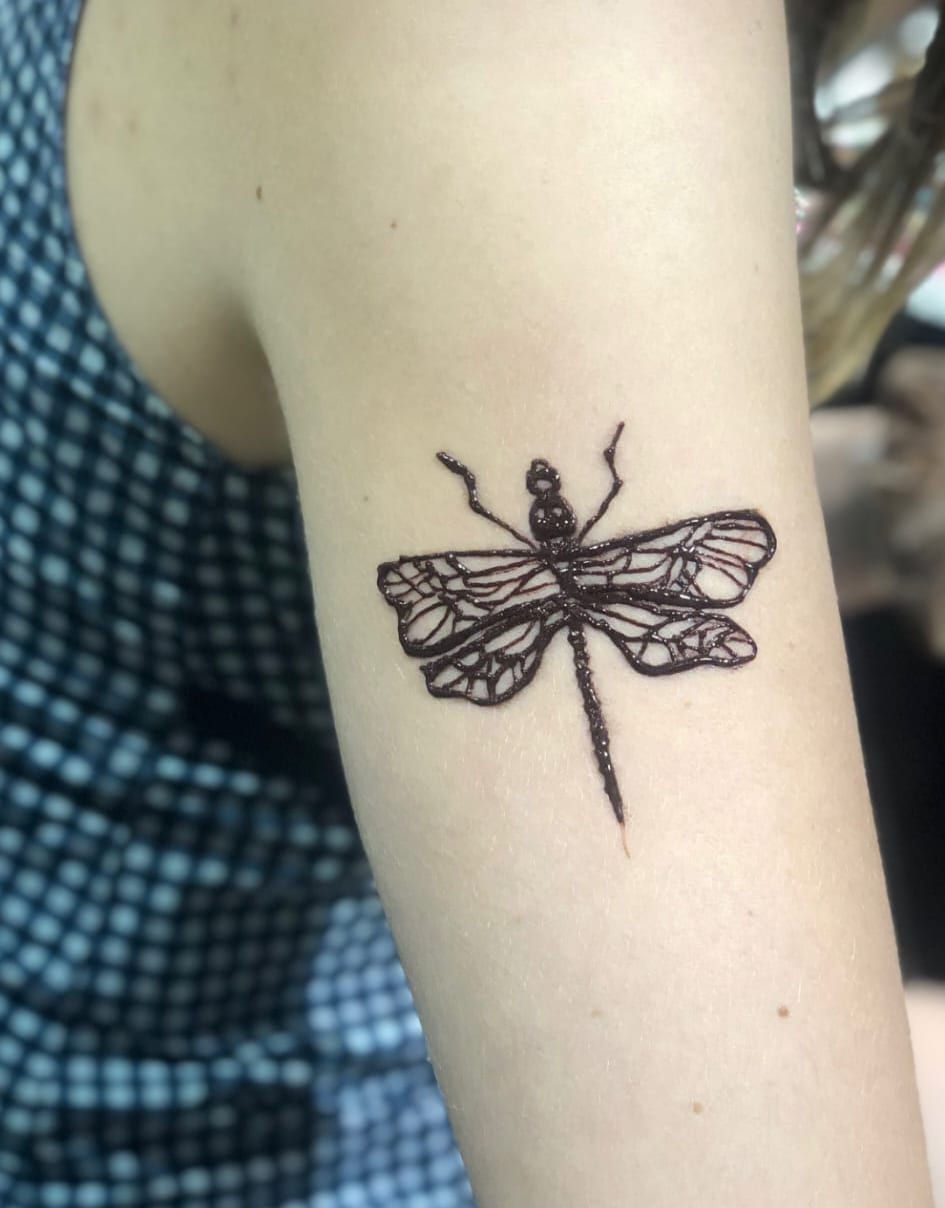 Fine-line dragonfly henna tattoo on the upper arm, Calgary