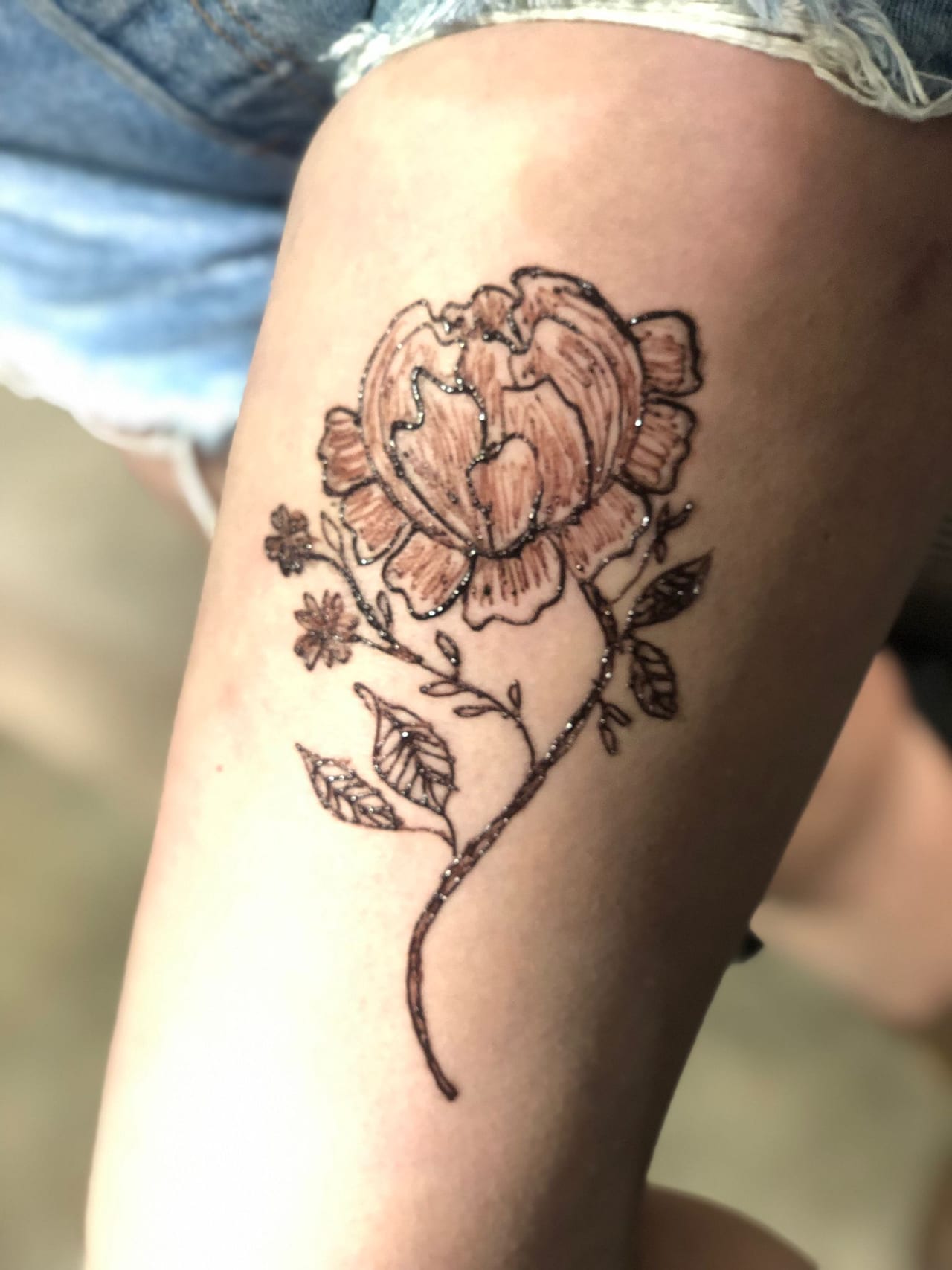 Peony and wildflower henna tattoo on a thigh with fine shading and glitter accents, Calgary